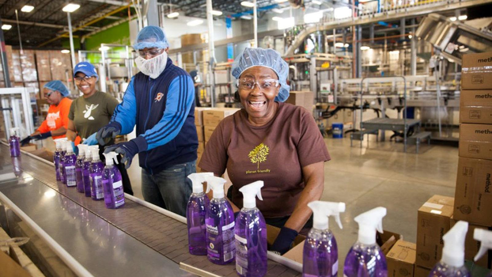 Medarbejdere med hårnet ved samlebånd med lilla sprayflasker