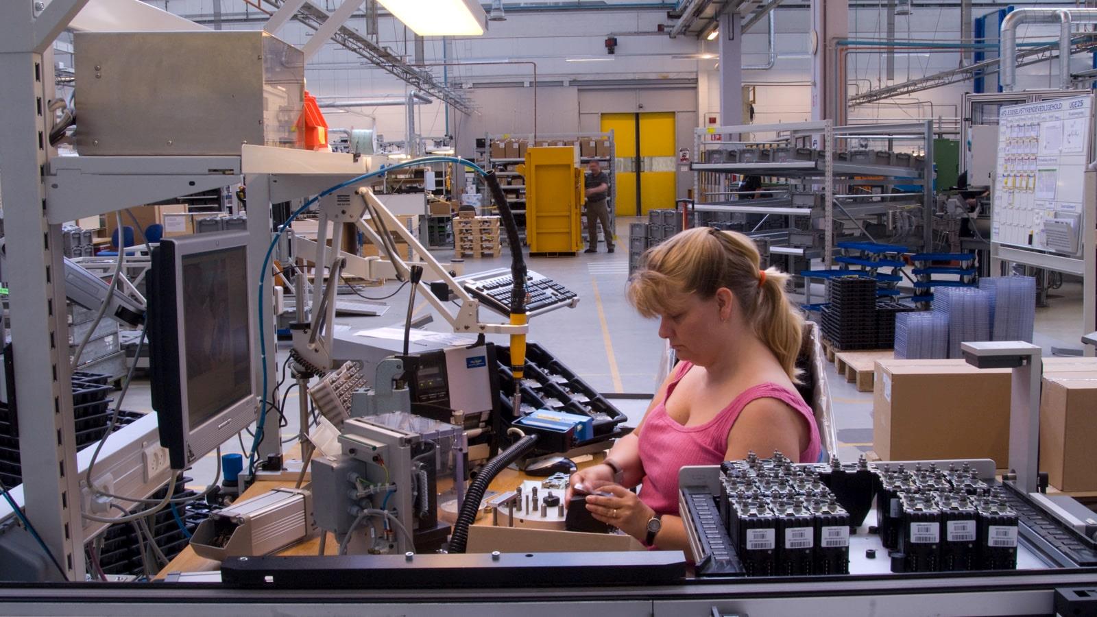 Blond kvinde i pink bluse arbejder ved samlebånd på Sauer-Danfoss