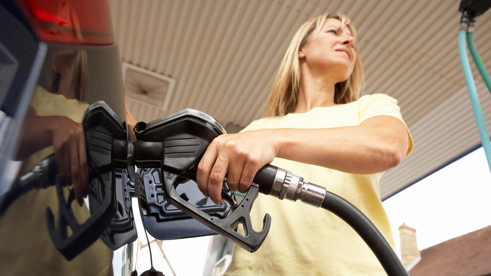 Langhåret kvinde fylder benzin i hendes sorte bil